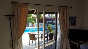 A room with a sliding glass door leading to an outdoor area with a pool, a chair, and a potted plant. - Wonderful villa with a large private heated pool and stunning views to the dunes (Corralejo)
