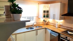 A modern kitchen with white cabinets, a double sink, a stove, and a dishwasher. - Wonderful villa with a large private heated pool and stunning views to the dunes (Corralejo)