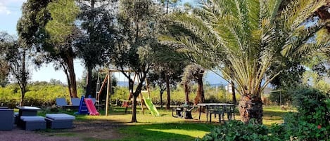 Un terrain de jeux avec des toboggans et des balançoires, entouré d’arbres et d’herbe.