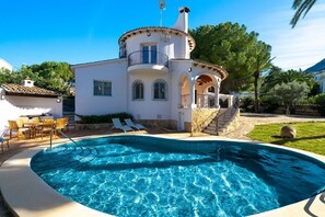A white villa with a pool, a balcony, and a staircase leading to a covered area.
