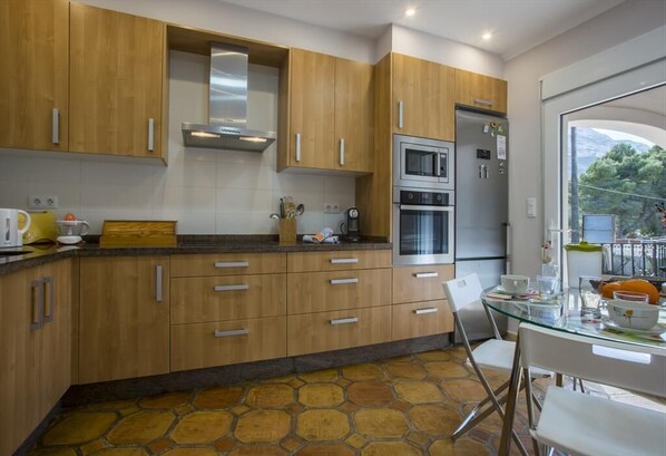 A modern kitchen with wooden cabinets, a glass dining table, and a stone-patterned floor.