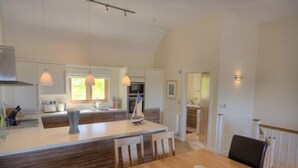 A spacious kitchen with a central island, pendant lighting, and a dining area with wooden furniture. - Beautiful holiday home, just a walk away from Talland beach... (Looe)
