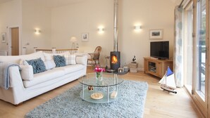 A living room with a white sofa, a glass coffee table, a fireplace, a television, and a large window. - Beautiful holiday home, just a walk away from Talland beach... (Looe)