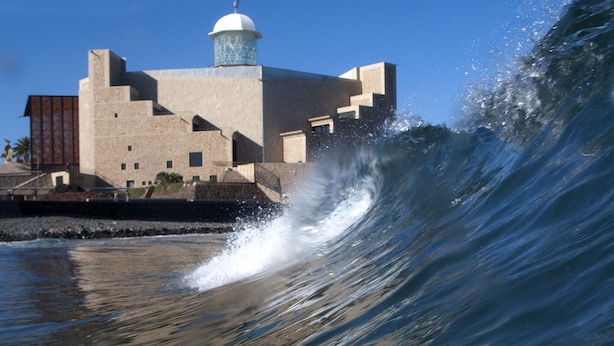 A building with a dome and a wave crashing in the foreground.