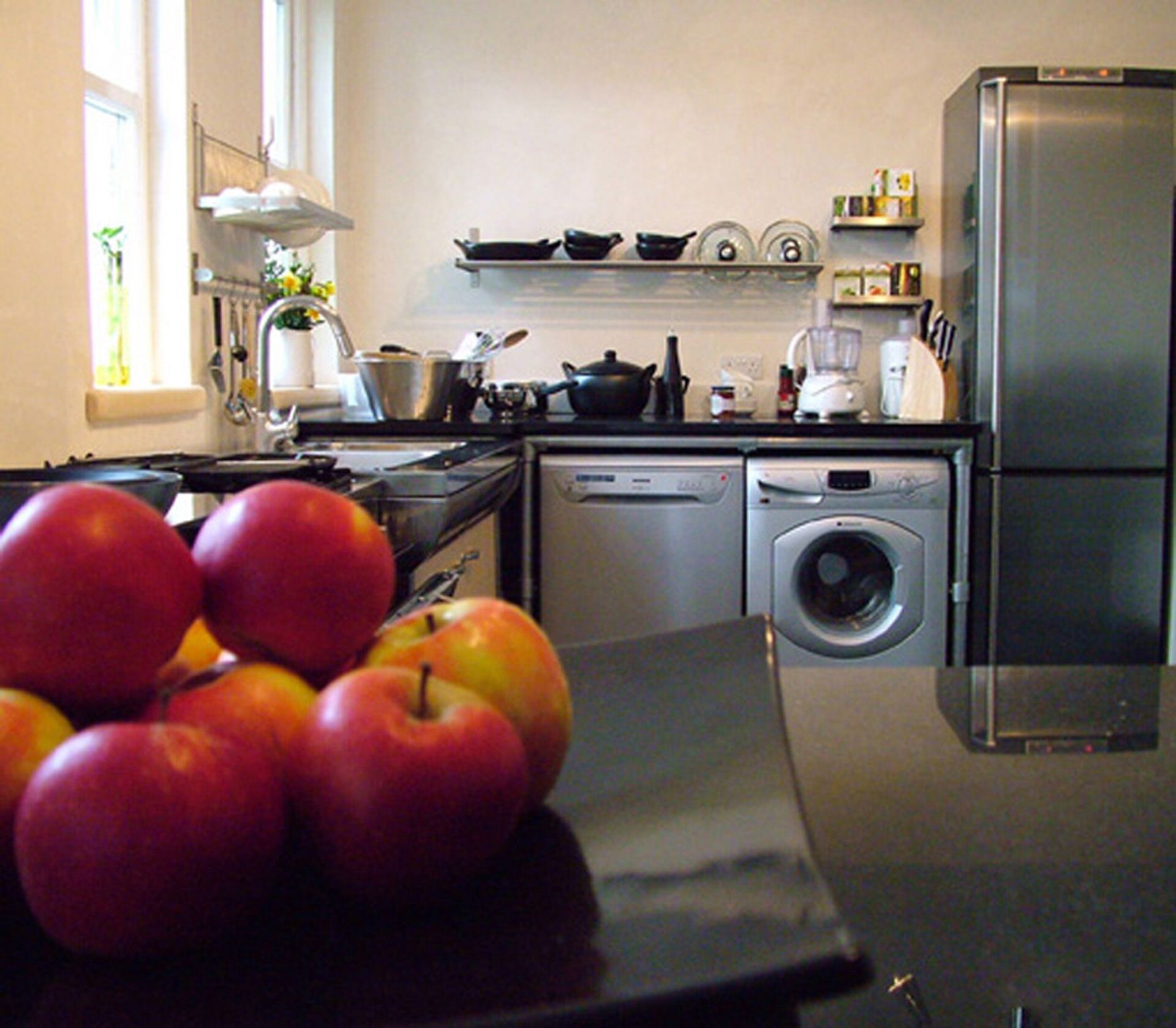 A kitchen with a refrigerator, dishwasher, stove, sink, and a bowl of apples on the counter.