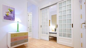 A room with a wooden floor, a white dresser with multiple drawers, a green lamp, and a bed with a white headboard.
