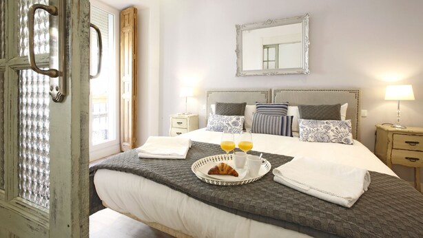 A neatly made bed with a tray of croissants and orange juice, a bedside table with a lamp, and a large mirror on the wall.