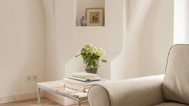 A minimalist room with a beige sofa, a small table with books and a plant, and a framed picture on the wall. - Apartment Gut Üselitz on Rügen - 1. First floor left (Poseritz)