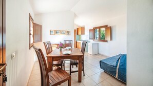 A dining area with a wooden table and chairs, a kitchen with wooden cabinets, and a blue sofa. - Nice home in Badesi OT with house sea view (Badesi OT)