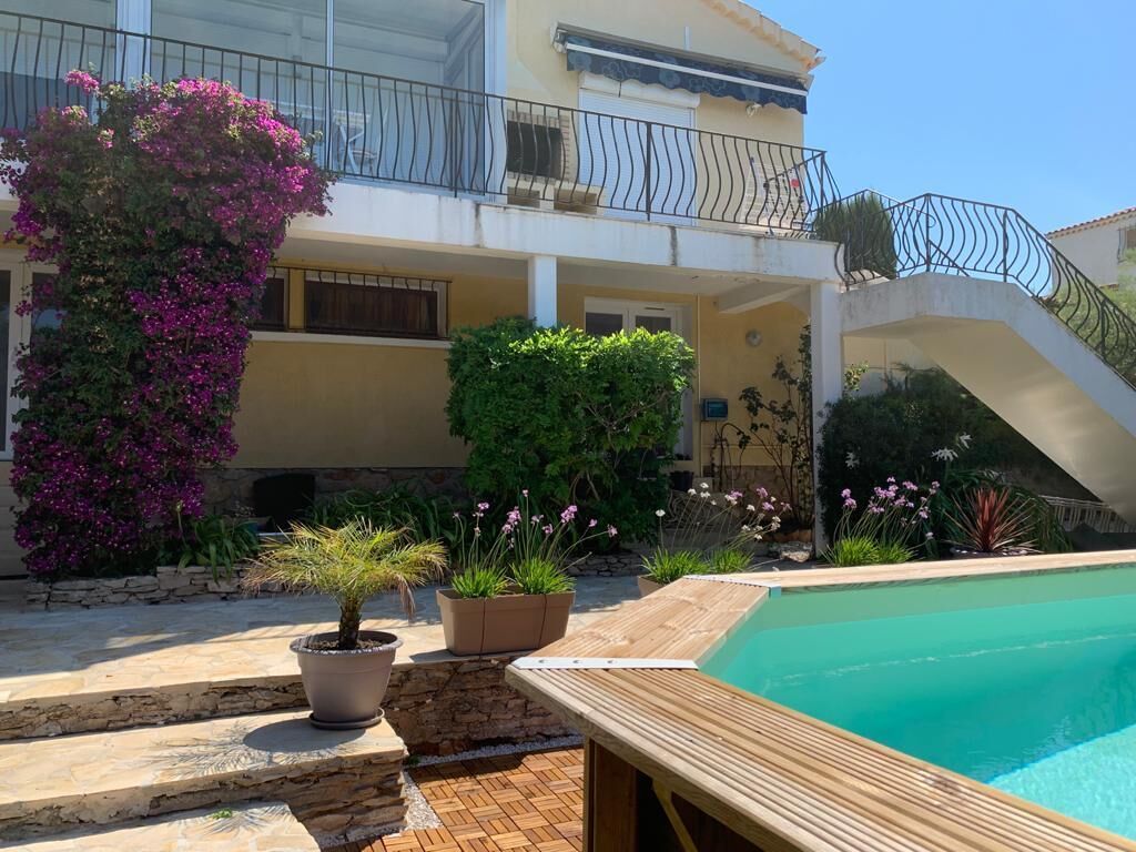 A pool area with a wooden deck, a small potted plant, and a staircase leading to a balcony with a railing.