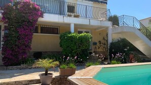 Un área de piscina con cubierta de madera, una pequeña planta en maceta y una escalera que conduce a un balcón con barandilla.