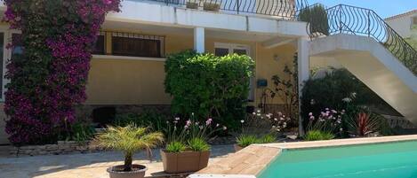 A pool area with a wooden deck, a small potted plant, and a staircase leading to a balcony with a railing.