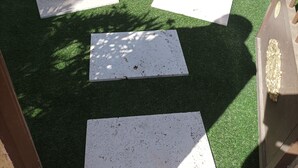 Un patio con césped artificial y losas de piedra dispuestas en un diseño.