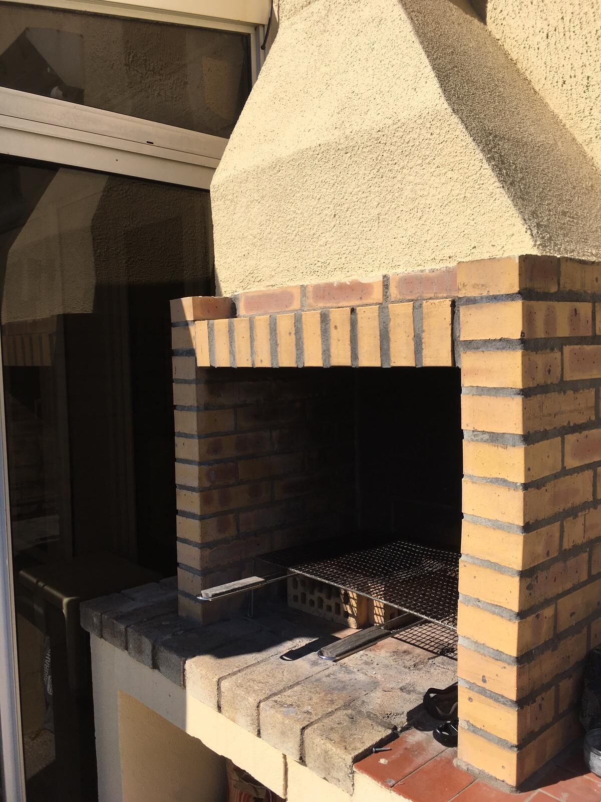 A brick-built outdoor oven with a metal grate, attached to a building with a window above.