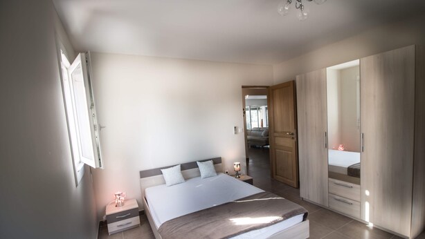 Un dormitorio con cama, mesitas de noche, armario y puerta que da a otra habitación.