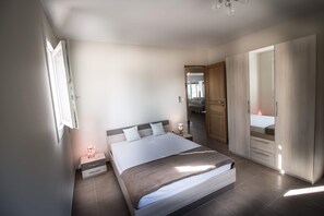 Ein Schlafzimmer mit einem Bett, Nachttischen, einem Kleiderschrank und einer Tür zu einem anderen Raum.