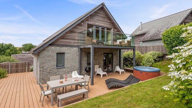 A modern house with a stone exterior, a wooden deck, a hot tub, and a glass-enclosed patio area.