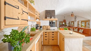 Ett kök med träskåp, en köksö och en sittgrupp med en soffa och kuddar.