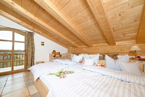 Un dormitorio con techo de madera, un ventanal con cortinas, una cama con ropa de cama a rayas y una mesita de noche con lámpara.