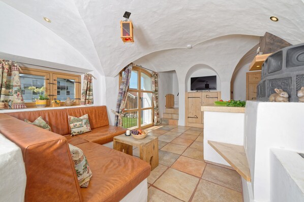 A cozy living room with a leather sofa, a small wooden table, and a kitchen area with a TV and wooden cabinets.