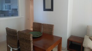 A dining area with a wooden table and wicker chairs, a green plate on the table, and a small side table with a pillow.
