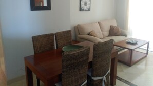 A dining area with a wooden table and wicker chairs, a beige sofa, and a small table with a plate.