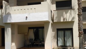 A modern building with a flat roof, a balcony with outdoor seating, and a palm tree.