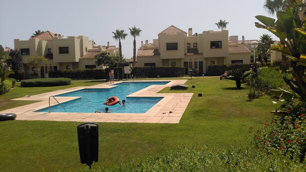 A swimming pool area with two pools, surrounded by well-maintained grass and palm trees.