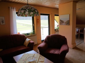 Un salón con dos sofás rojos, una mesa con posavasos, una lámpara de vitral y vistas a un paisaje verde por la ventana.