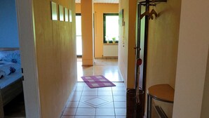 Un pasillo con una cama, un radiador, un perchero y una puerta que da a otra habitación.