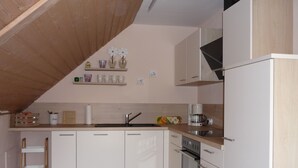 Una cocina con armarios blancos, techo de madera, horno empotrado y cafetera.