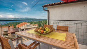 Un balcon avec une table dressée pour deux personnes, un parasol rouge et une vue sur la mer et les montagnes.