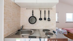 Une cuisine de taille réduite, équipée d’une cuisinière, d’un évier et d’ustensiles suspendus.