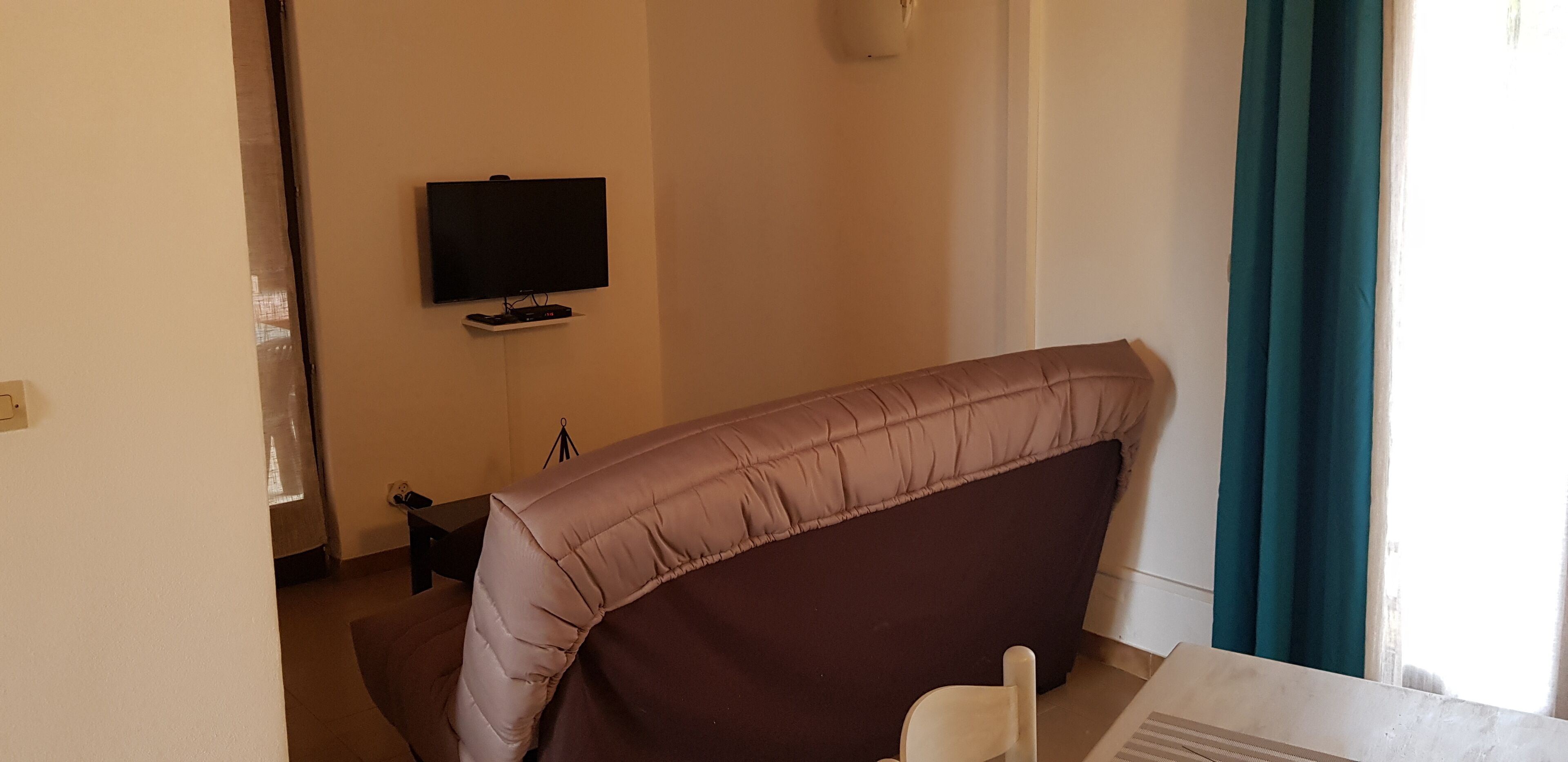 A room with a bed, a television on a stand, a small table, and a window with curtains.