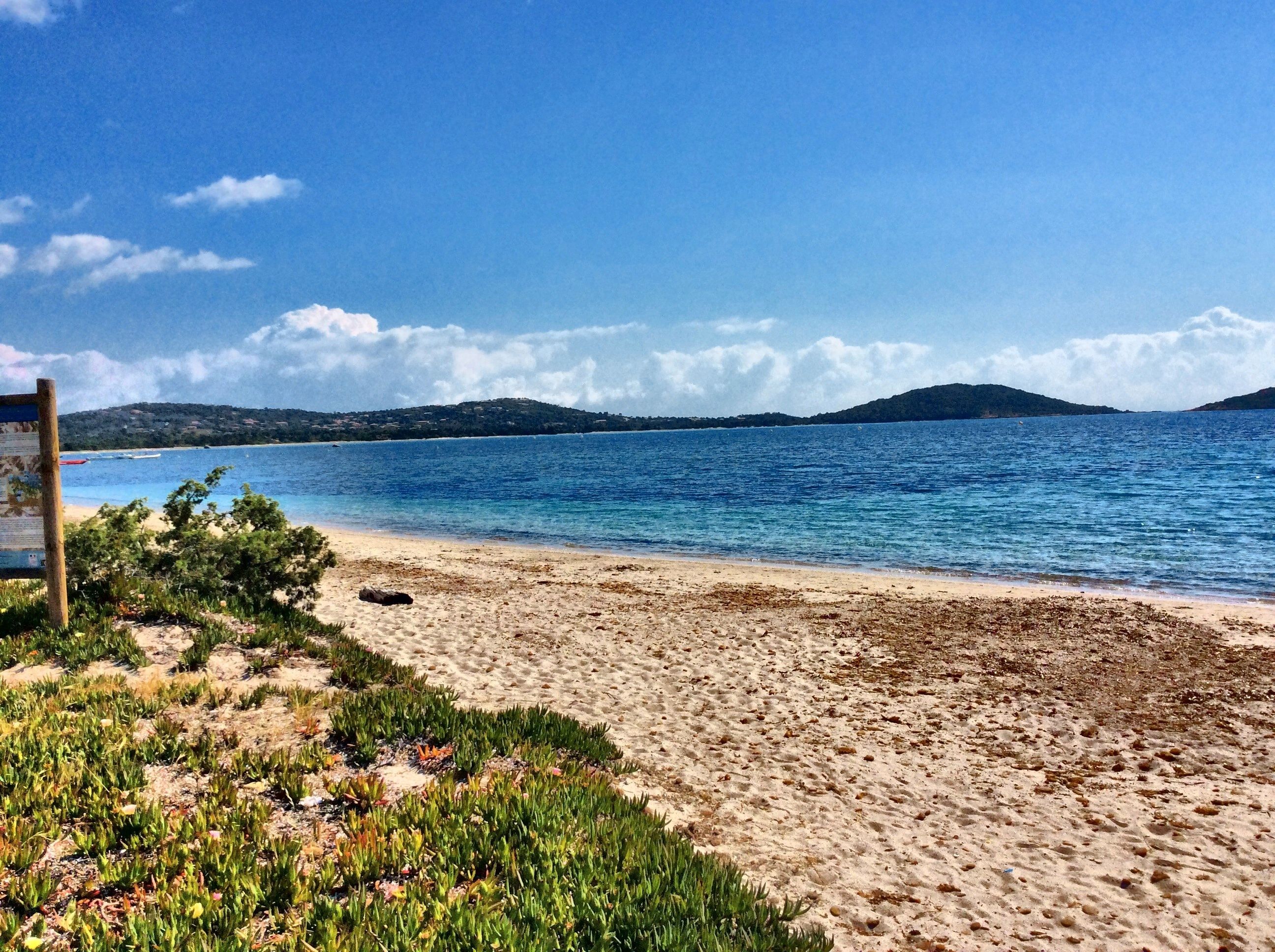 Una spiaggia con acqua cristallina, una riva sabbiosa e un cartello.