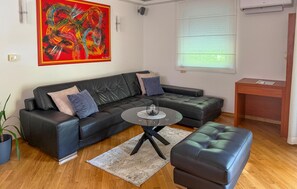 A living room with a black leather sofa, a round coffee table, and a blue ottoman.