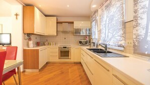 Een moderne keuken met witte kastjes, een houten eettafel met rode stoelen en een groot raam met een muurschildering van bomen.