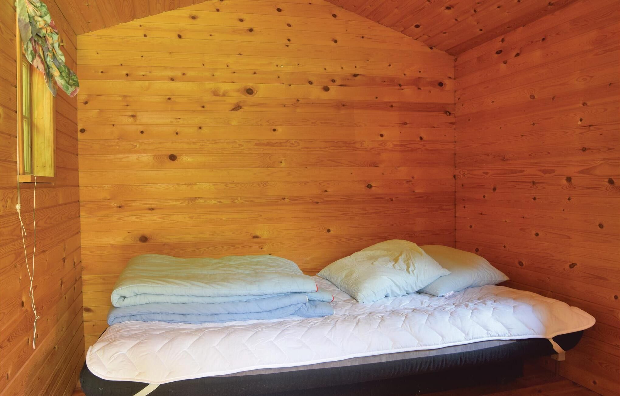 Ein Zimmer in einer Holzhütte mit einem Bett, Kissen und einem Fenster mit Vorhängen.