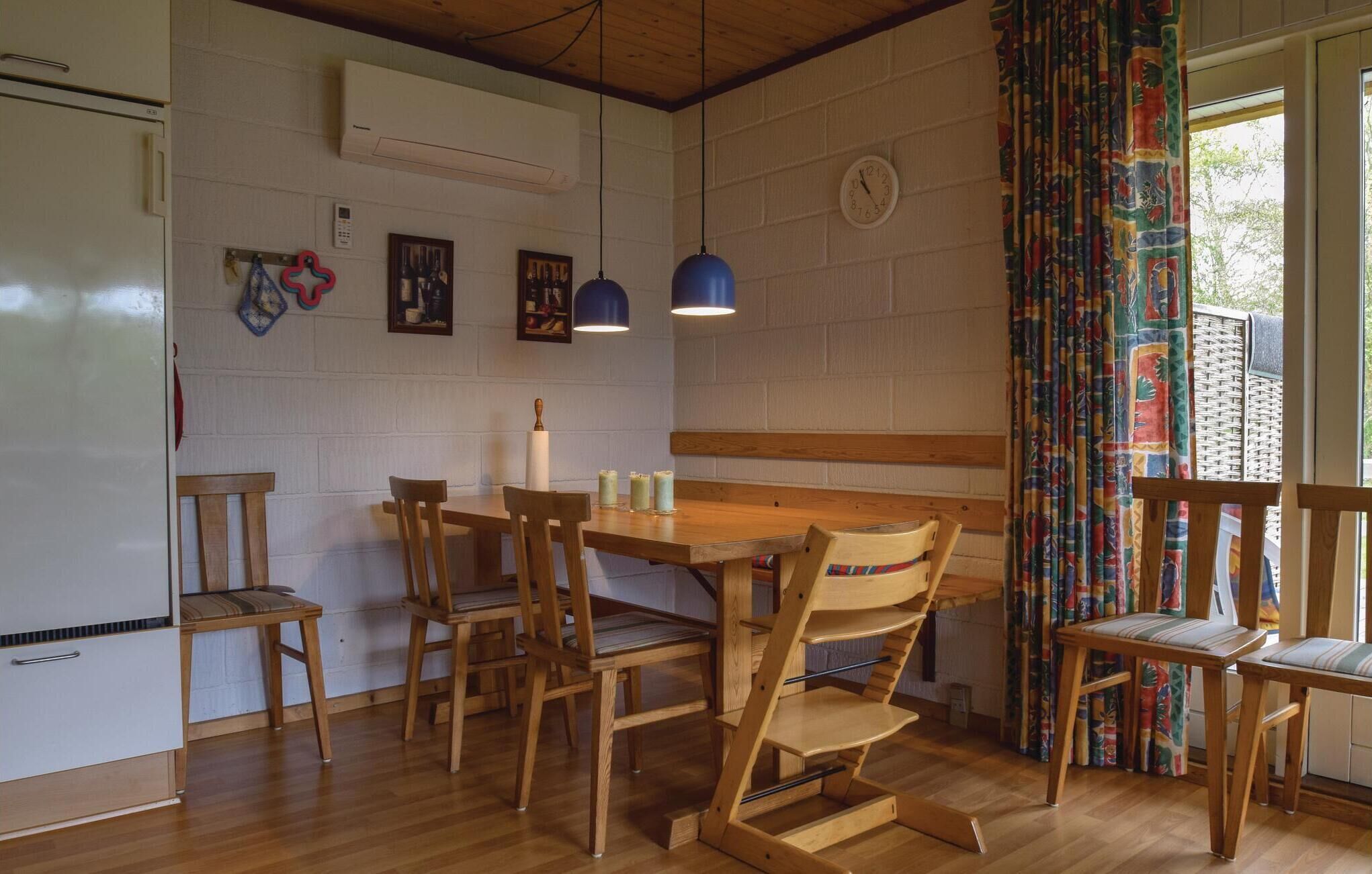 Een gezellige keuken met houten meubels, een eettafel en een bankje. Er is een koelkast, een airconditioning en een klok aan de muur.
