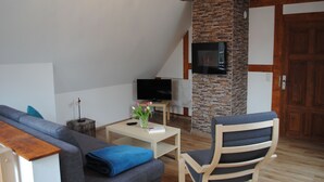 Un salon moderne avec un mur d’accent en pierre, un téléviseur à écran plat, un canapé, un fauteuil et une petite table sur laquelle est posé un vase de fleurs.