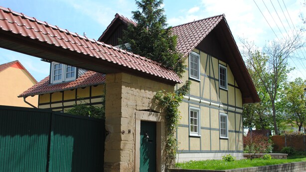 Une maison traditionnelle à deux étages, avec un toit recouvert de tuiles, une porte verte et un petit jardin.