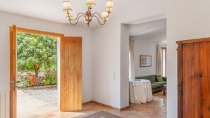 A spacious hallway with a wooden door leading to a garden, a chandelier, and a green sofa in the background. - 784524 Ses Cases, Spain (Manacor)