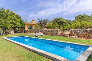 Una piscina rectangular con un muro de piedra y un césped.