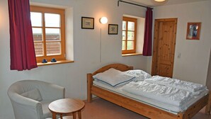 A bedroom with a wooden bed, two chairs, a small round table, and two windows with curtains. - 01 Holiday apartment Gänseblümchen with lake view - Haus am Höft in Gager with lake view (Gager)