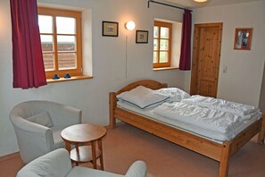 A bedroom with a wooden bed, two chairs, a small round table, and two windows with curtains.