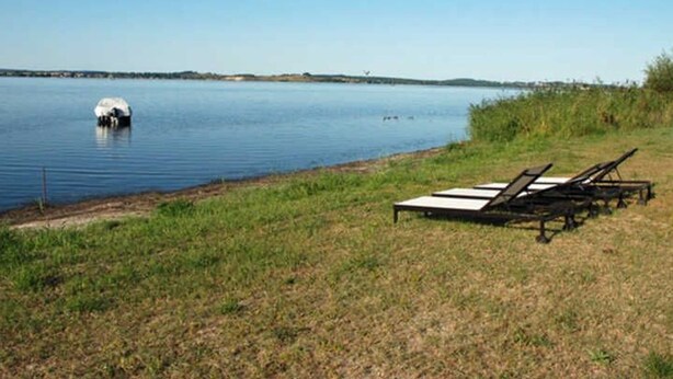 A lakeside view with lounge chairs and a small boat. - 01 Holiday apartment Gänseblümchen with lake view - Haus am Höft in Gager with lake view (Gager)