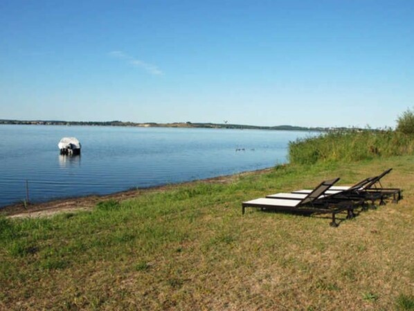 A lakeside view with lounge chairs and a small boat.