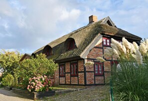 A traditional half-timbered house with a thatched roof, red windows, and a stone chimney.