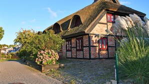 A traditional half-timbered house with a thatched roof, a cobblestone driveway, and a flower bed with pink flowers. - 01 Holiday apartment Gänseblümchen with lake view - Haus am Höft in Gager with lake view (Gager)