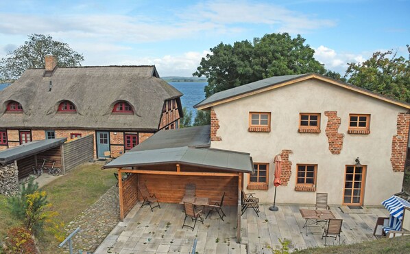 A house with a thatched roof and a brick facade, a covered patio with outdoor furniture, and a view of the water.